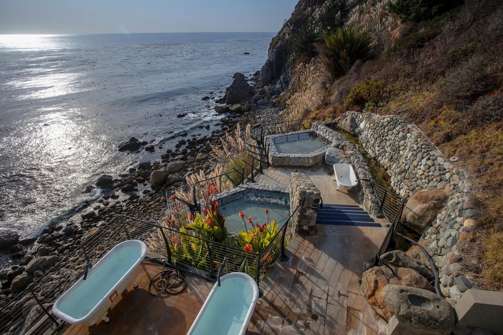 Outdoor stone soaking pools and clawfoot tubs on a cliff above the ocean